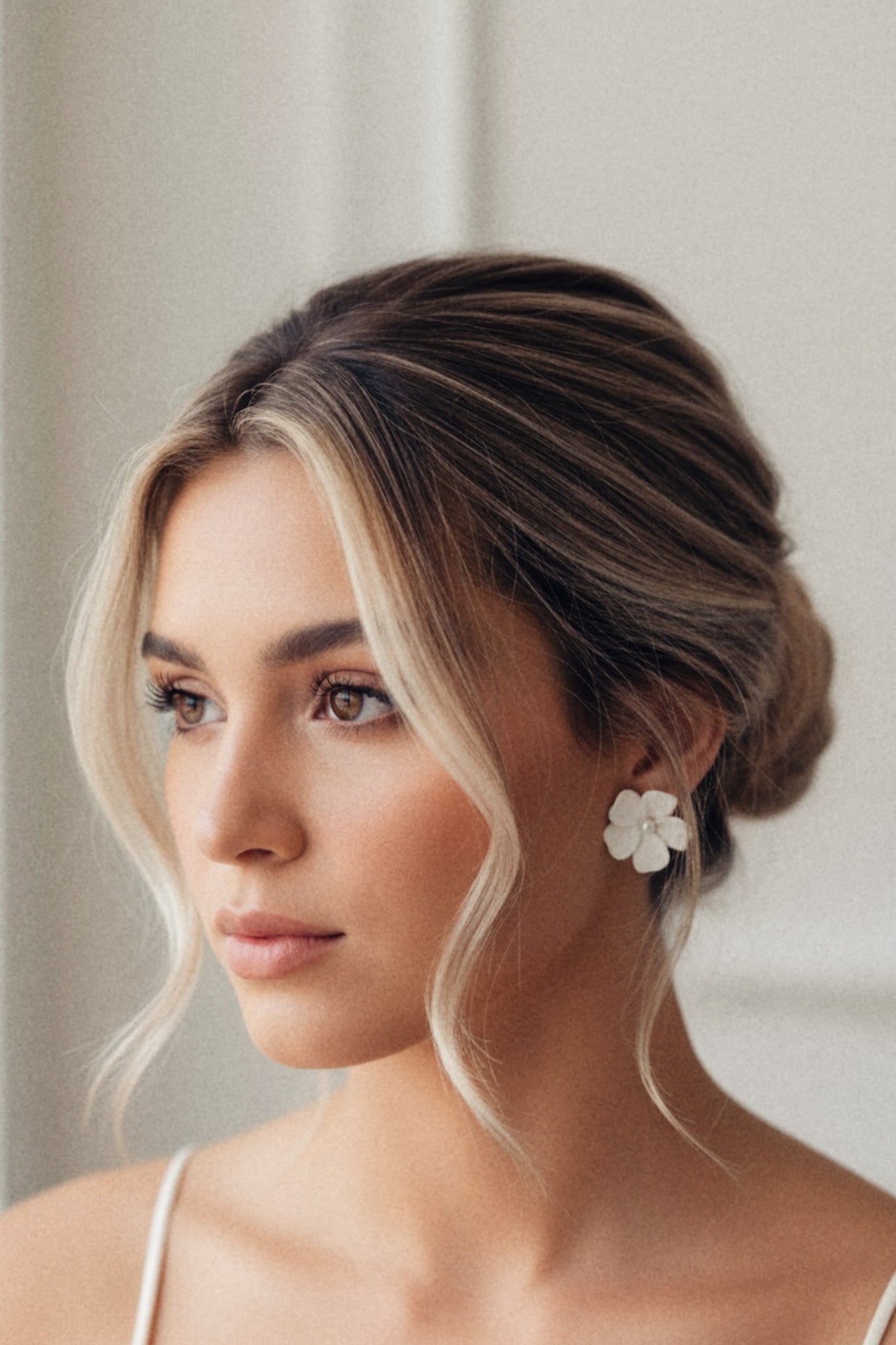 Woman with styled hair and floral earrings against a neutral background