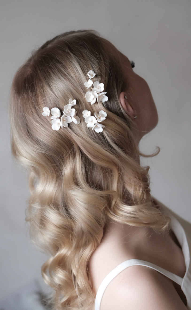 Woman with blonde hair styled with white floral hair accessories against a neutral background
