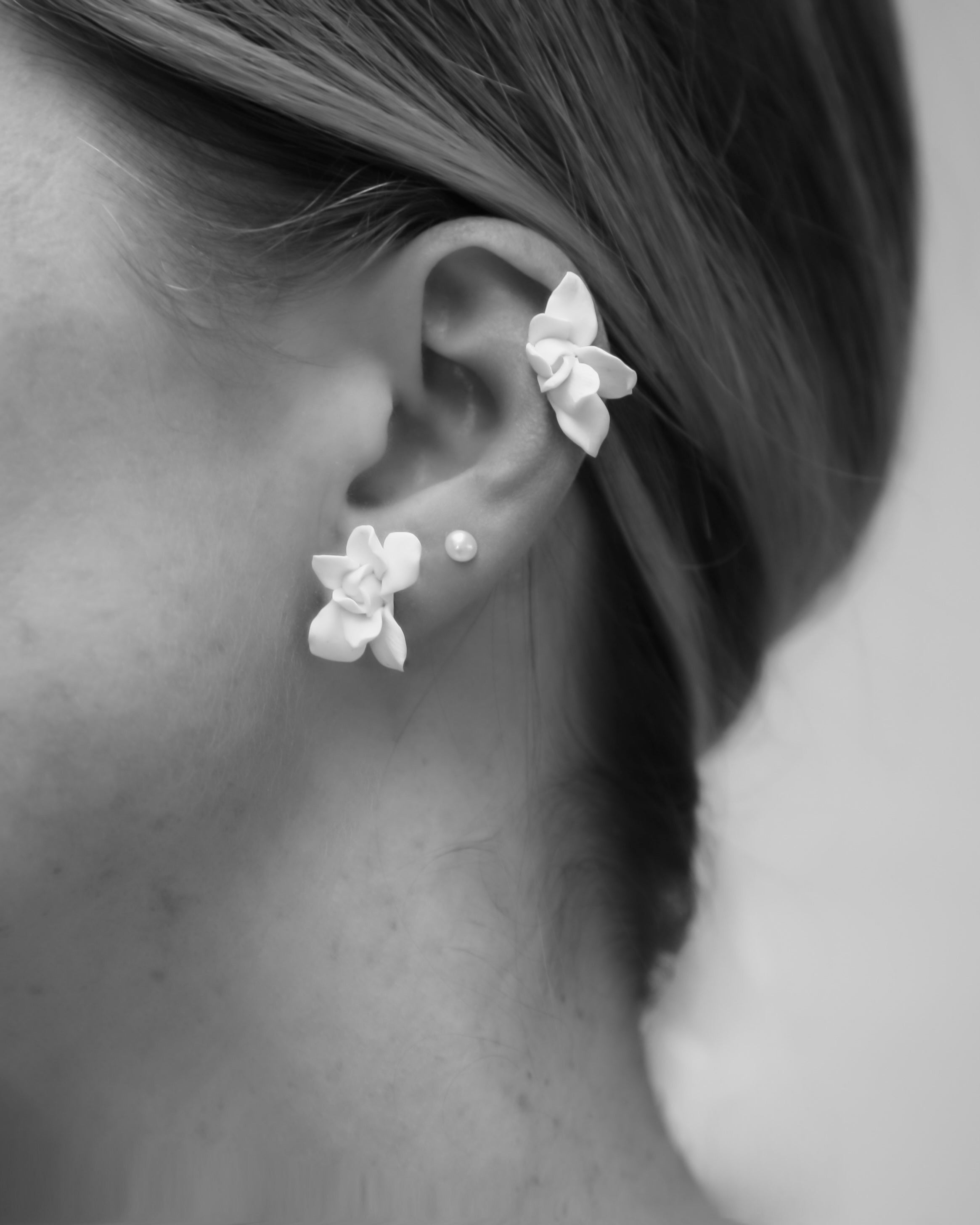 Close-up of an ear wearing white floral earrings with a blurred background